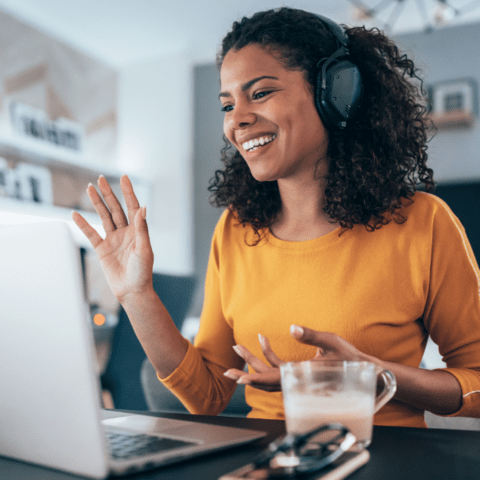 Woman wearing headphones and waving at a computer camera