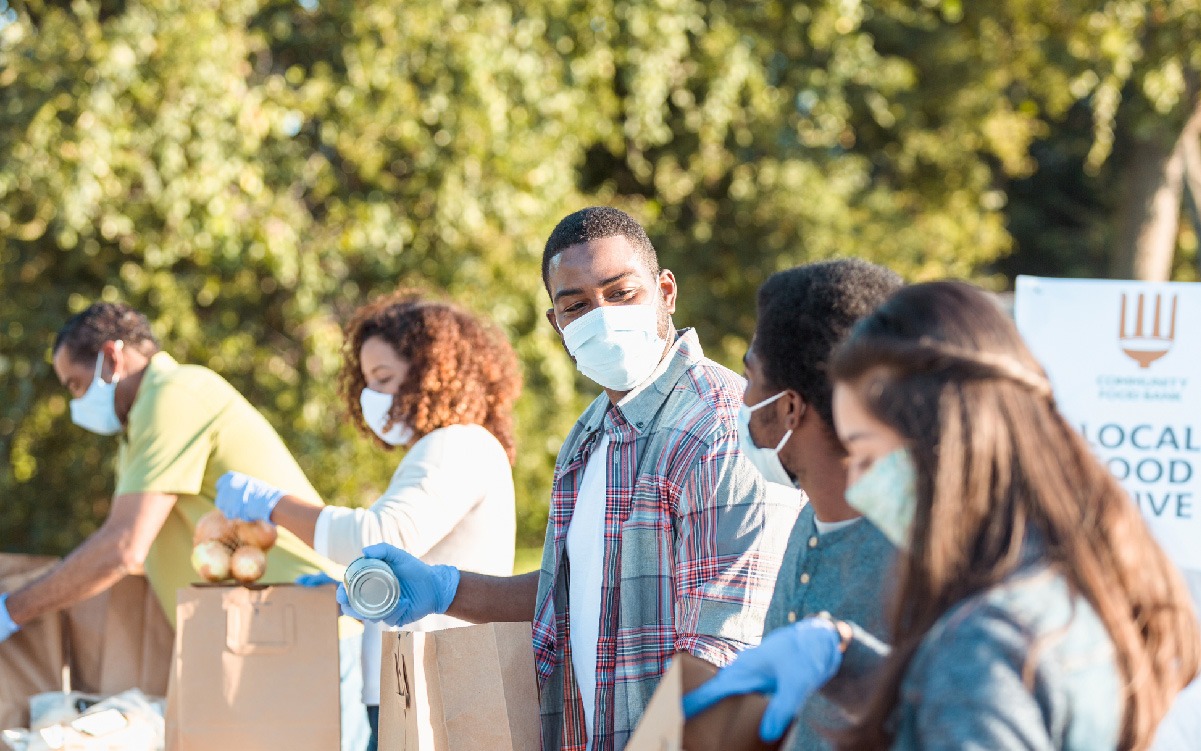 Line of people wearing masks put grocery items into bags