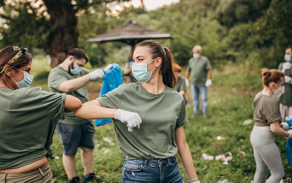 Two women wearing masks and bumping elbows while picking up trash with a group