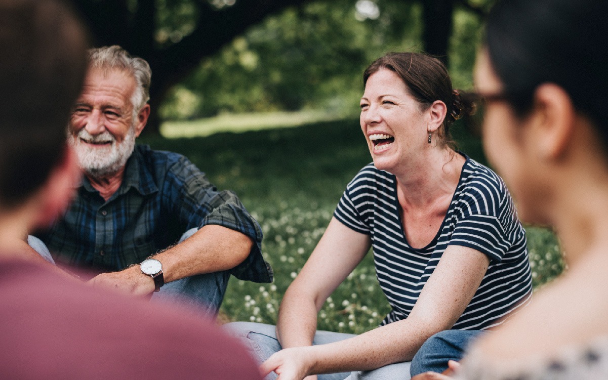 Group of people sitting in the grass, with a woman and man smiling