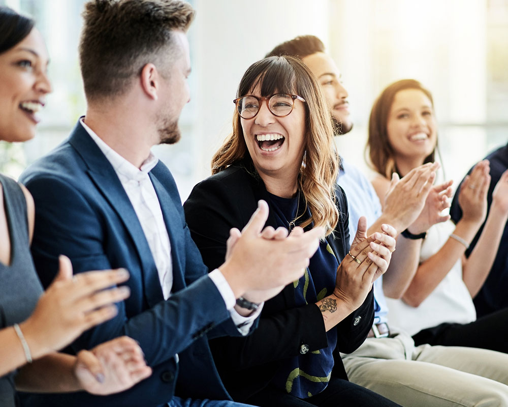 Group of employees sitting together, smiling and clapping