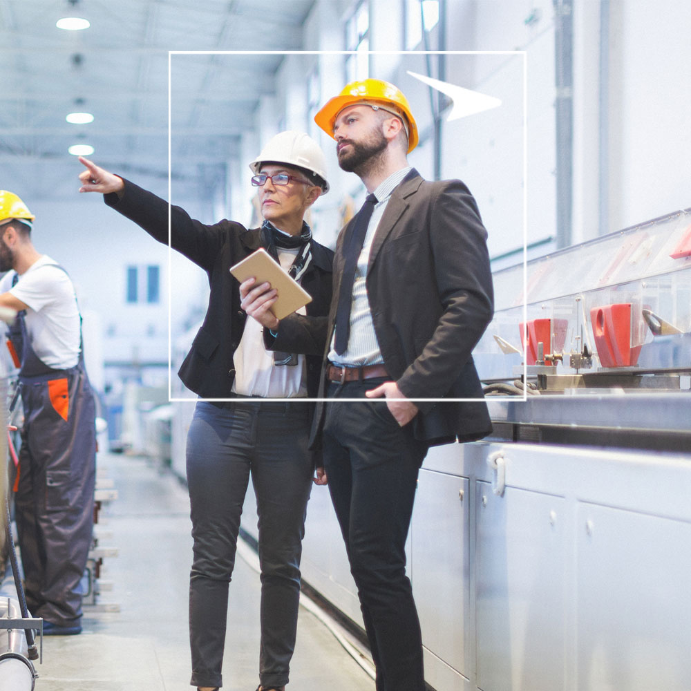 Two coworkers in hard hats and suits against warehouse background