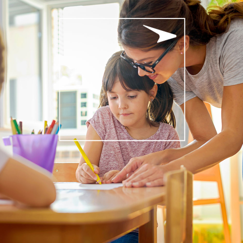 Teacher helps girl student write in classroom