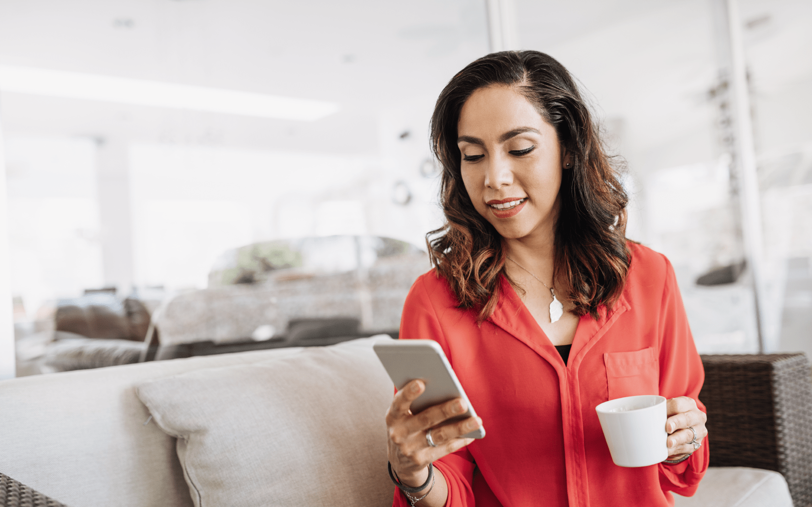 Woman holding phone and coffee cup on living room couch