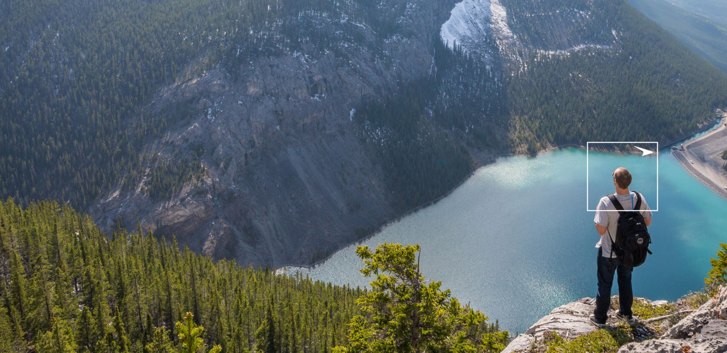 Man with a backpack standing on a cliff overlooking trees and water