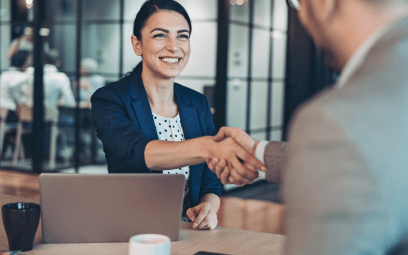 Woman in professional attire smiling and shaking a man's hand