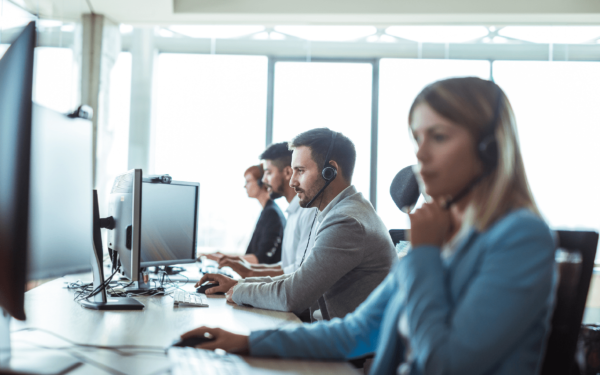 Row of people at desks in a call center, wearing headsets and working at monitors