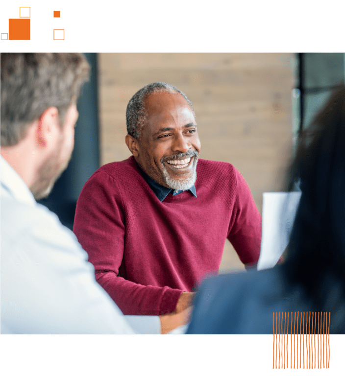 Older man smiling and sitting with coworkers in an office
