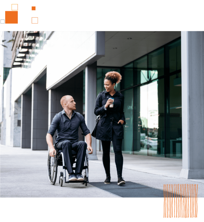 Woman holding coffee walking next to man in wheelchair on sidewalk outside of office building