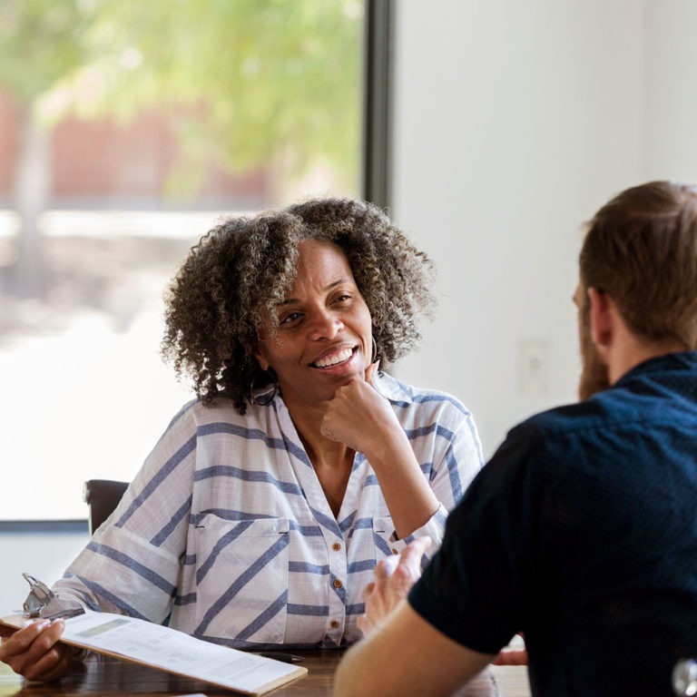 Woman sitting at desk interviewing job candidate with clipboard