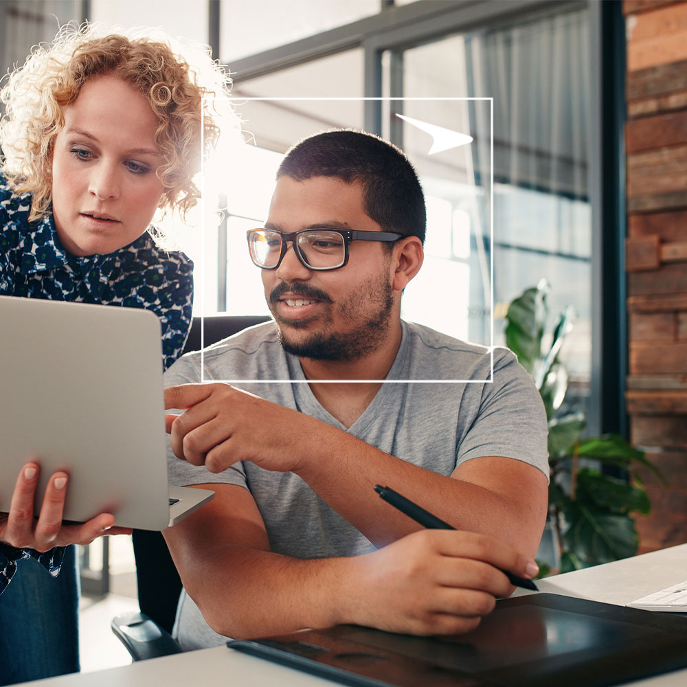 Two coworkers looking at laptop against office background