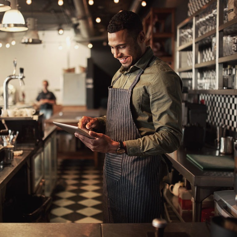 Man in apron behind bar counter holding tablet