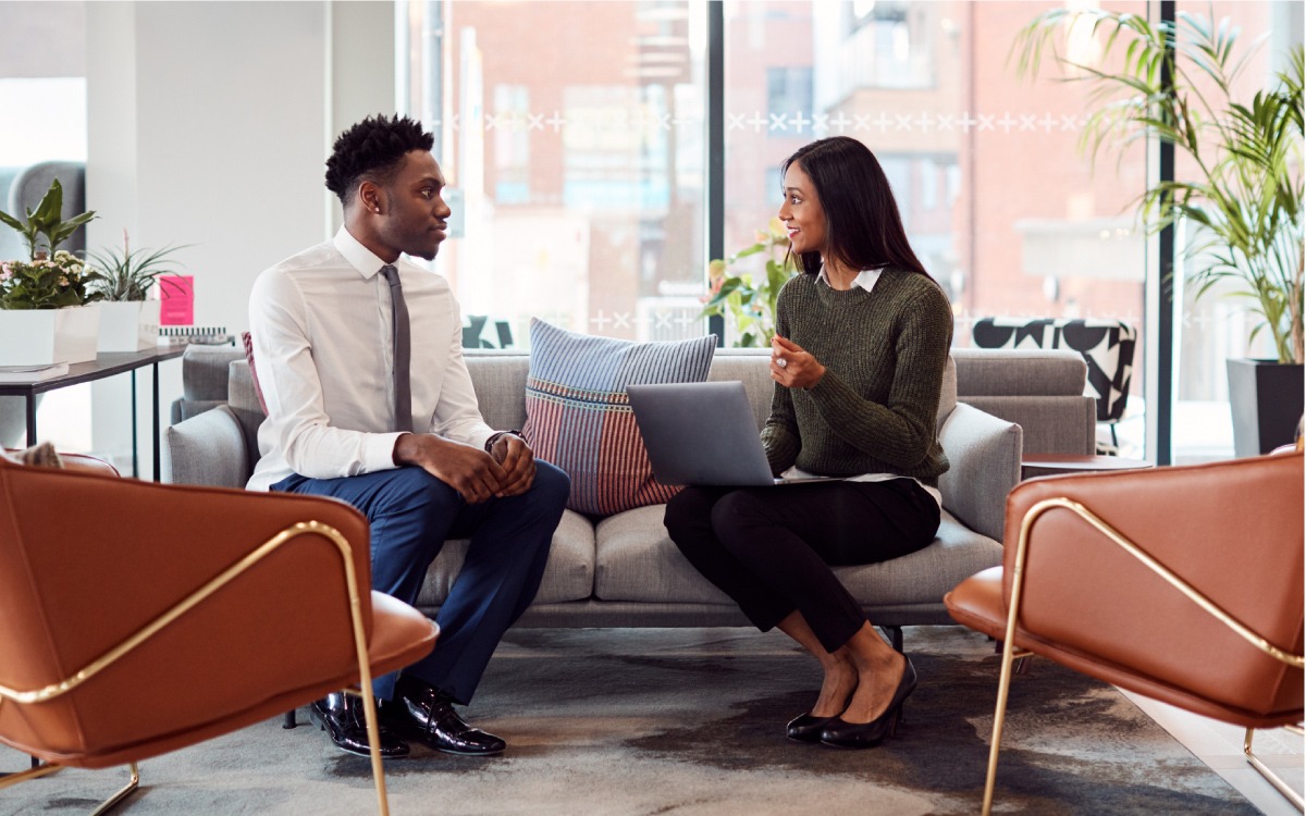 Woman with laptop computer interviewing man with suit on couch