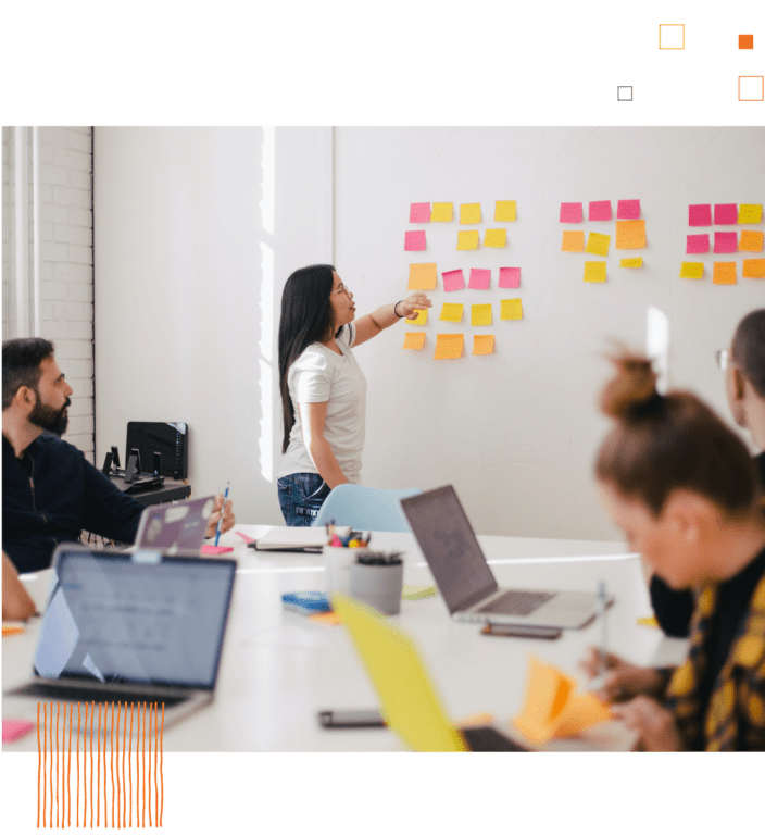 Woman placing sticky notes on white board in front of coworkers at table