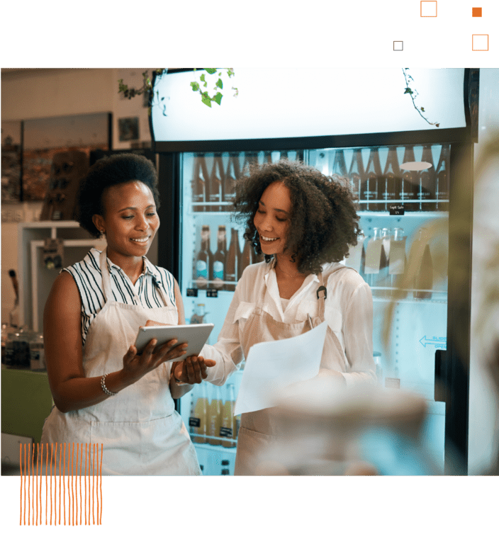 Two women in aprons looking at tablet against food retail background