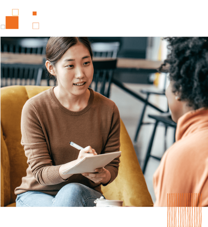 Two women sitting on office chairs and writing on notepad