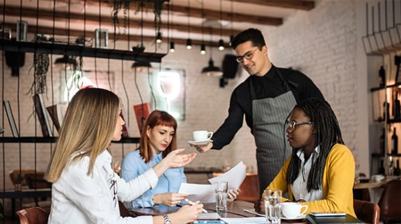 server handing coffee cup to customer at table