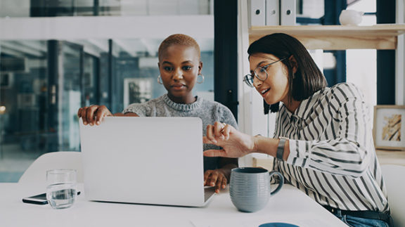 two professional women conferencing around a laptop