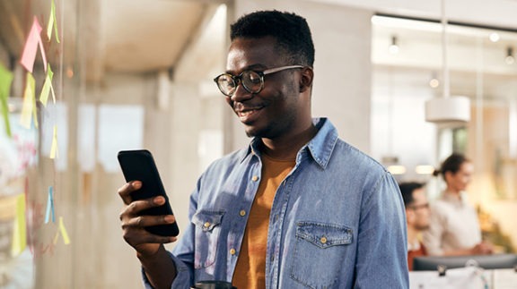 young man smiling at his phone in front of post it wall