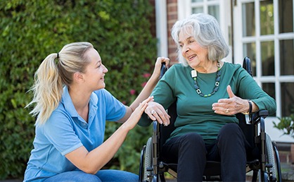 woman kneels down to talk to elderly woman in a wheelchair