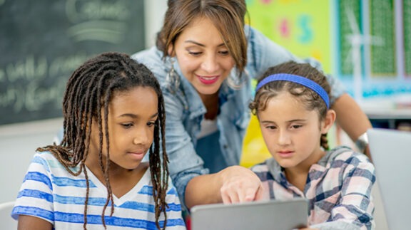 woman leaning over point at a screen with 2 kids