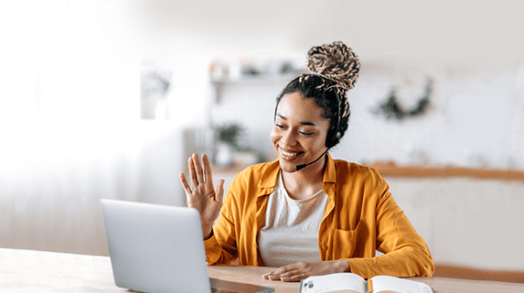 woman with bun sitting at computer using headset and waving to screen