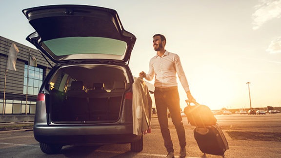 man with luggage and coat getting into a car