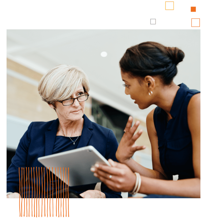 two women sitting and talking in front of a tablet