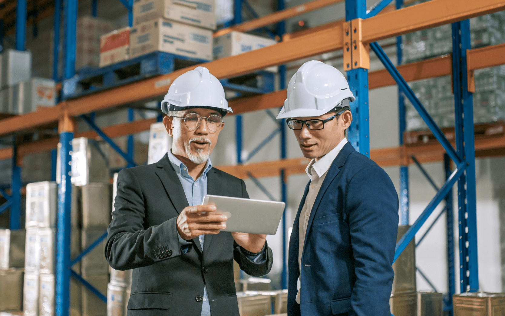 two business men in hard hats of warehouse looking at tablet