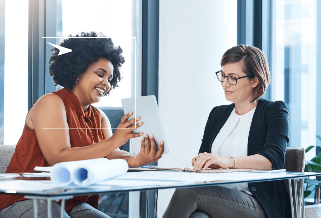 two professional women sitting at a table looking at a tablet