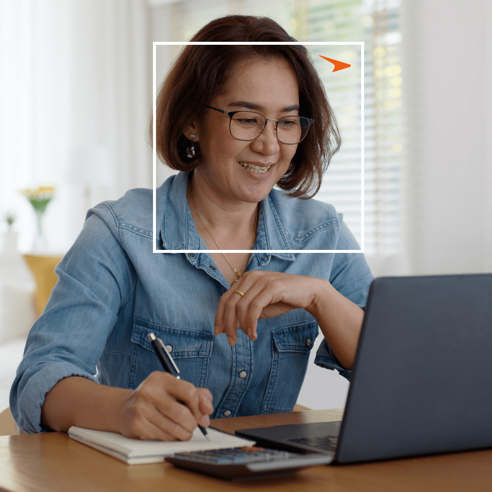 woman in a jean shirt taking notes in front of a laptop