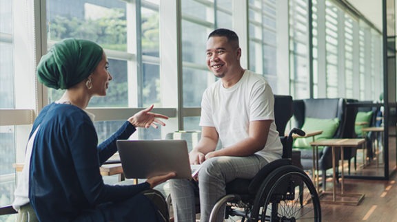 man in wheelchair talking to woman holding laptop