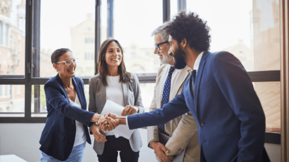 2 professionals shaking hands while two others look on smiling