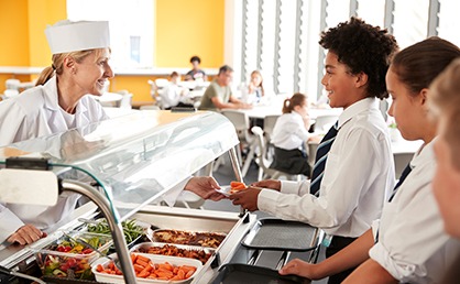 worker in school cafeteria handing food to student