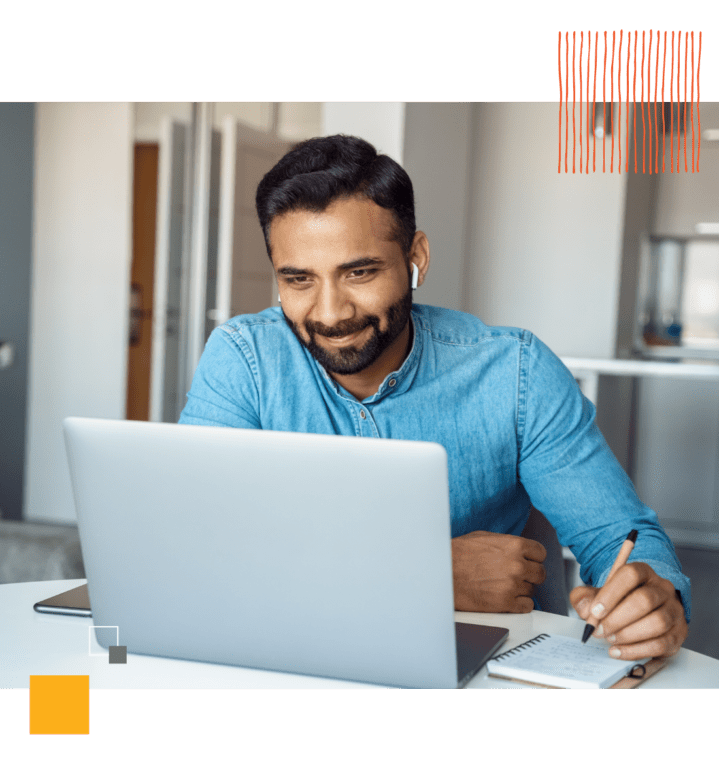 man taking notes as he looks at laptop