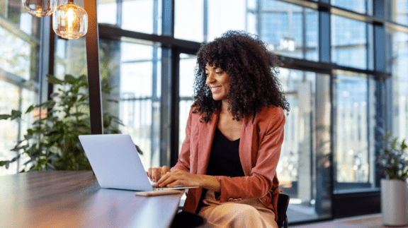 woman in a salmon blazer sitting at table on laptop