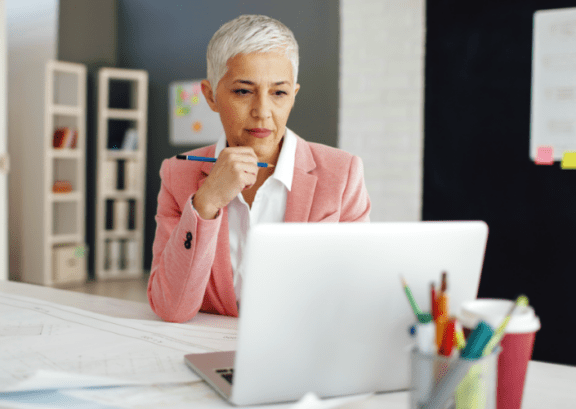 woman looking at laptop with pen in hand