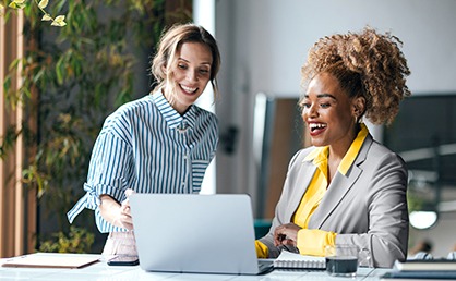 two women in office smiling as they view a computer together