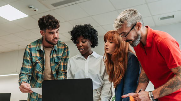 Employees collaborating around a laptop to review HR technology solutions in an office.